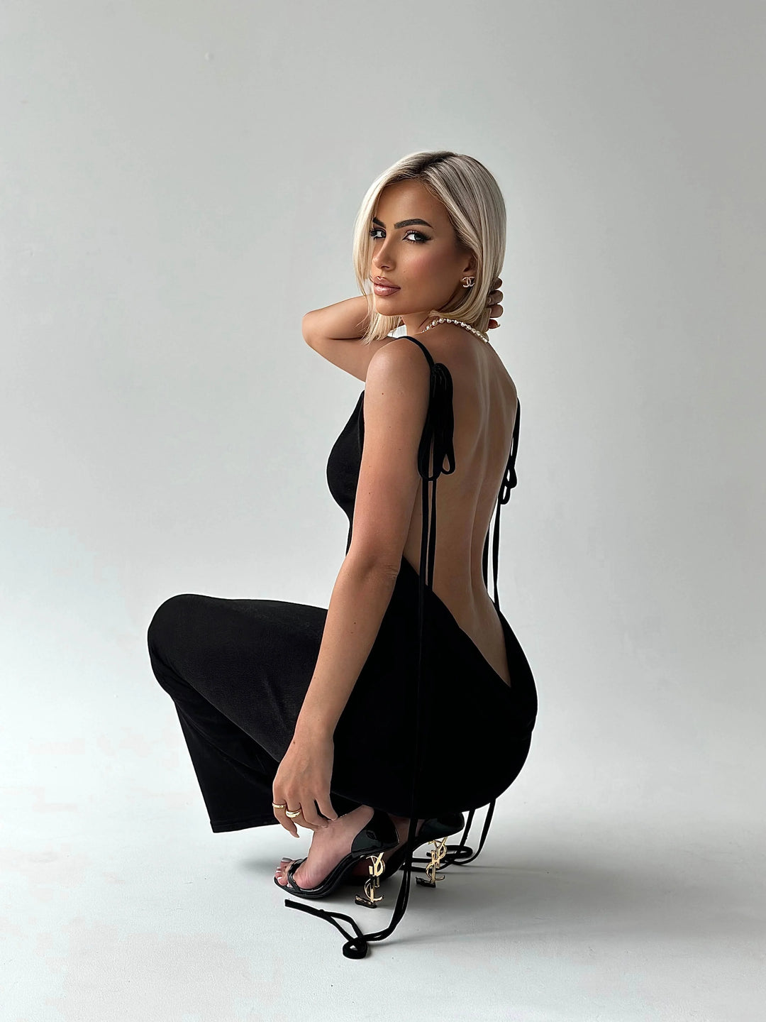Black backless dress with adjustable ties, made of soft, stretchy fabric. Sleek design with modern twist perfect for any…