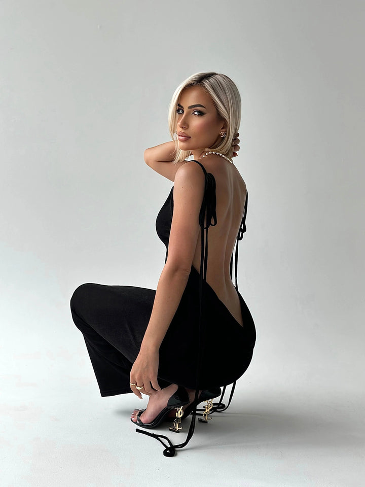 Black backless dress with adjustable ties, made of soft, stretchy fabric. Sleek design with modern twist perfect for any…
