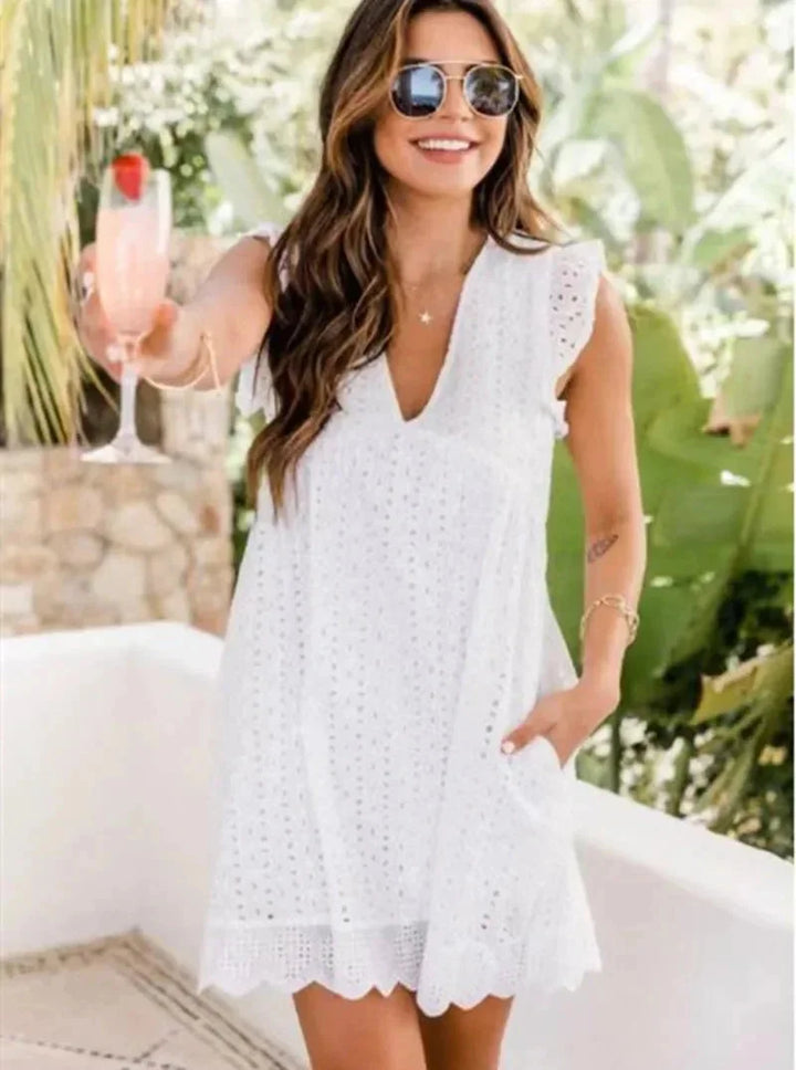 White eyelet mini dress with a flowy silhouette, featuring a V-neck design. Feminine and airy, perfect for summer days or…