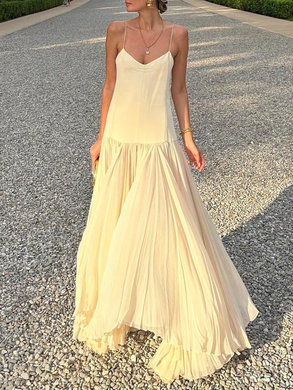 Sleeveless ivory pleated maxi dress with a flowing silhouette and intricate pleating detail.