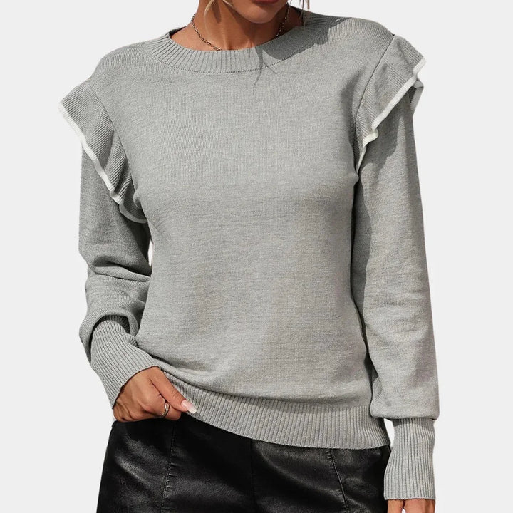 Grey ruffle-trimmed crewneck sweater by Amaya. Soft knit fabric with elegant ruffle detailing along neckline, capturing a…