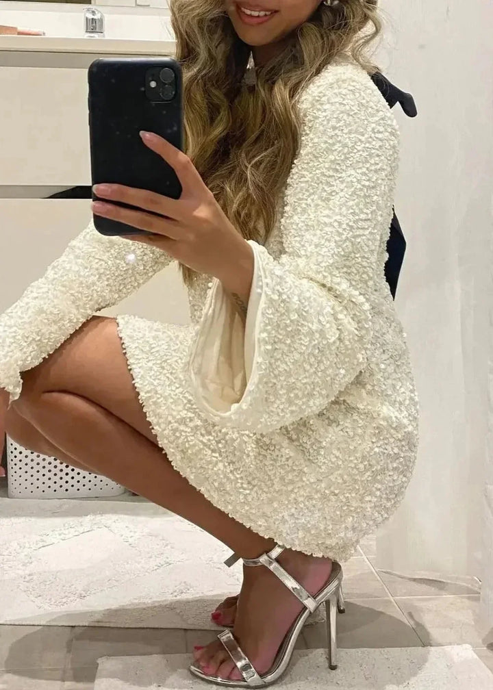 White mini dress featuring elegant neckline detail, sparkling fabric, and sleek design by Atalia.