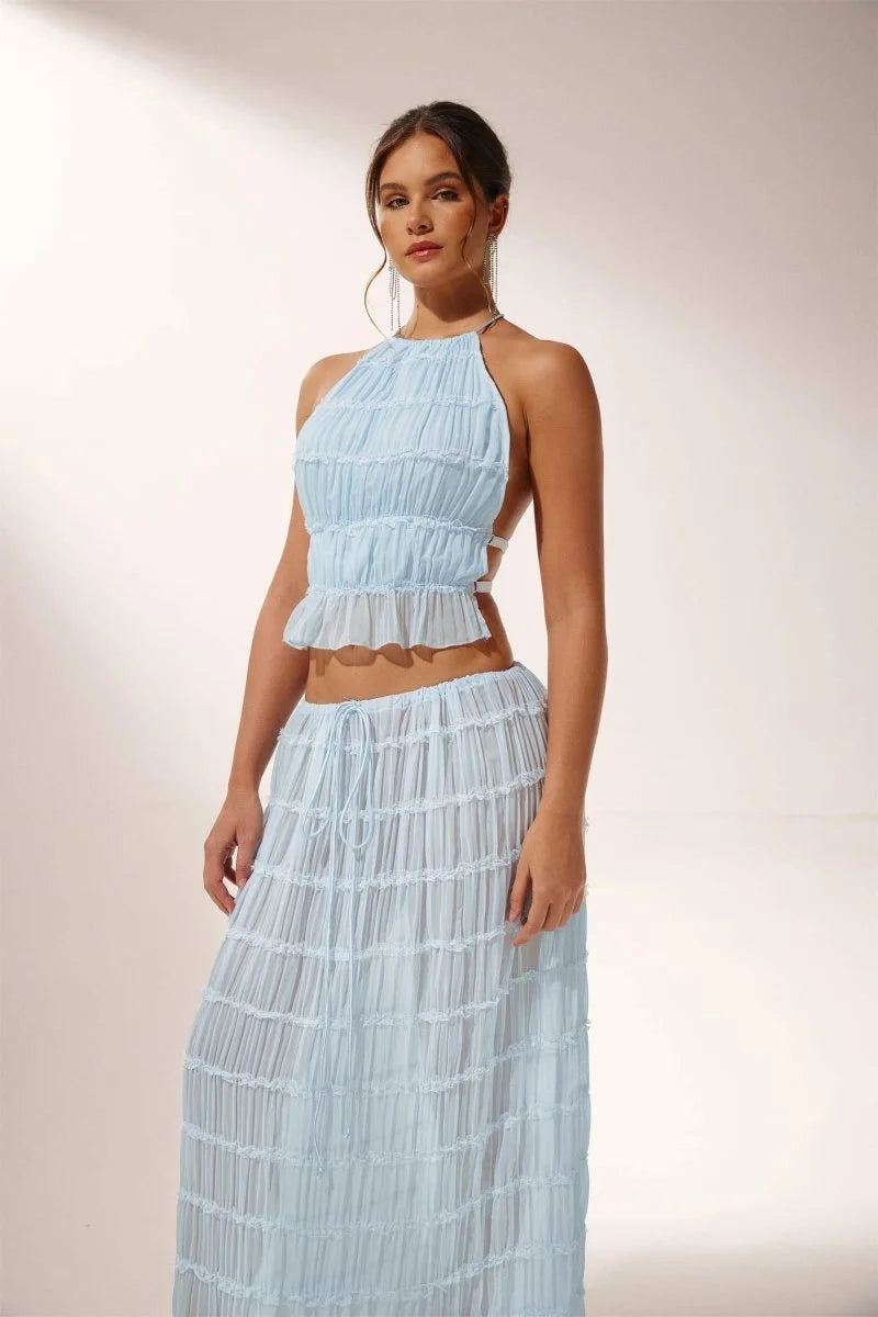 Light blue pleated halter crop top and skirt set. Features a flowy design perfect for summer, made from a comfortable fabric.