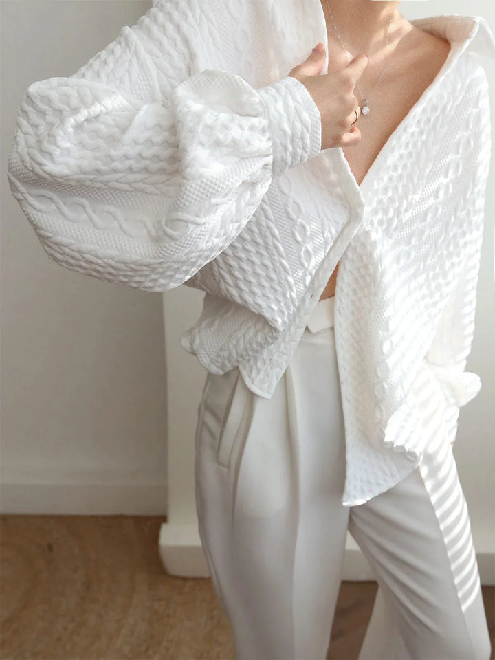 White long-sleeve blouse with textured fabric and sculpted sleeves, perfect for adding a touch of elegance to your outfit.