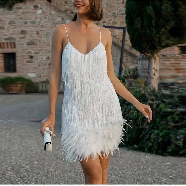 White mini dress with spaghetti straps, adorned with sequins and feathers. Ideal for a chic and elegant look at any event.