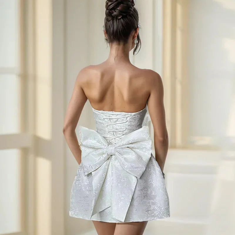 "Strapless mini dress in candy pink with oversized bow detail, perfect for summer occasions."