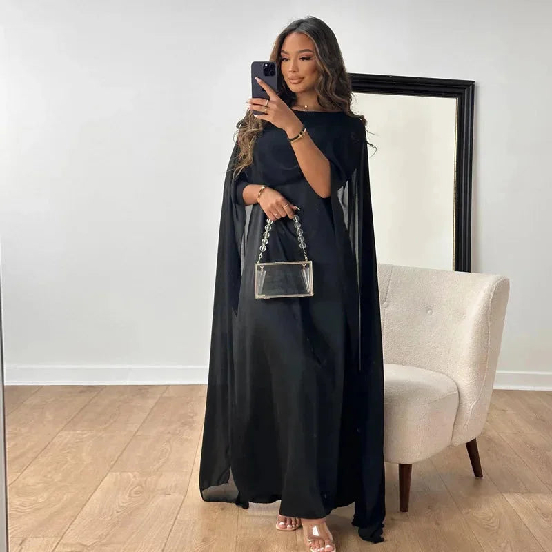 Black cape maxi dress for evening wear, featuring a flowing design with an elegant cape detail. Made from high-quality,…