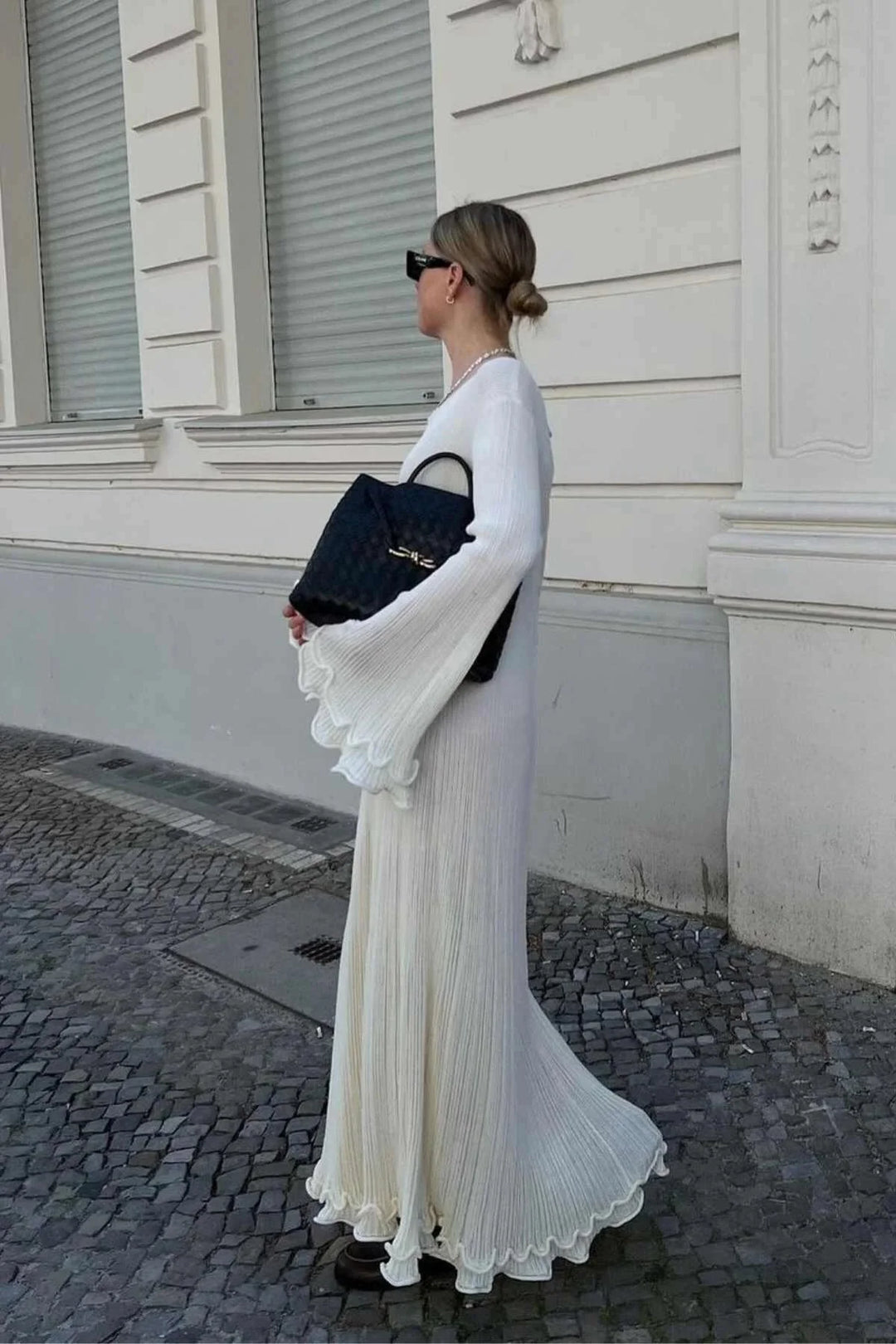 "White floor-length dress with bell sleeves, made from pleated fabric, elegant and timeless design."