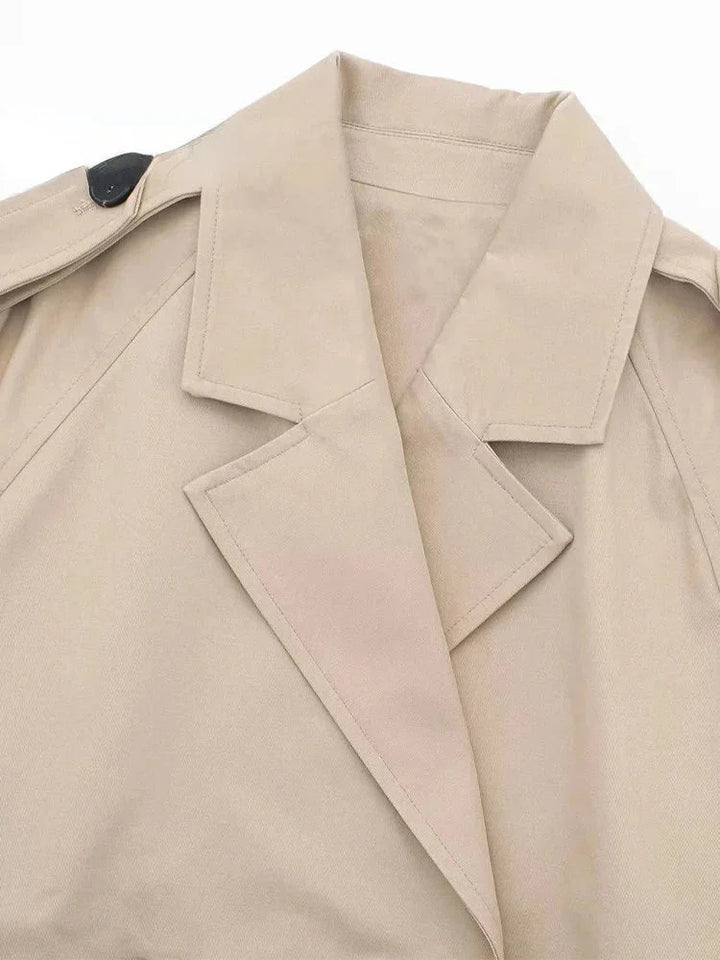 Beige cropped trenchcoat with buckle detailing, structured silhouette and wide lapel collar.