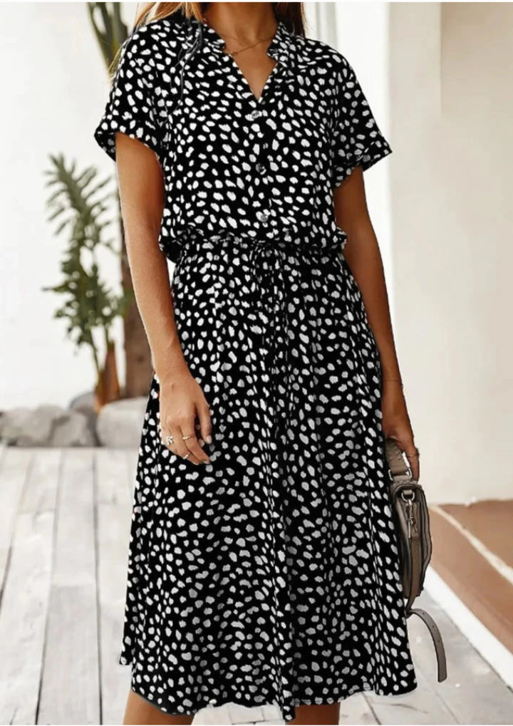 Black midi dress with white polka dots, featuring a waist tie. Flattering silhouette suitable for various occasions.